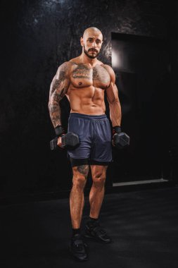 Spor salonunda dambılla ağır antrenman yaparken poz veren genç bir fitness oyuncusunun fotoğrafı..