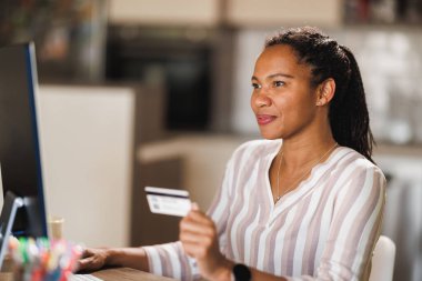Afrikalı iş kadını ev ofisinde otururken elektronik bankacılık veya çevrimiçi alışveriş için bilgisayar kullanıyor.