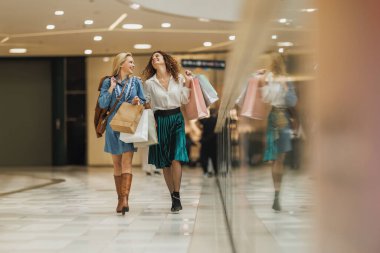 Gün içinde alışveriş merkezinde alışveriş torbalarıyla yürürken gülümseyen iki çekici kız arkadaşın fotoğrafı..