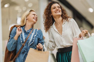 Alışveriş torbaları taşıyan ve Kara Cuma ya da Siber Pazartesi satışları sırasında alışveriş merkezinde gülümseyen iki güzel kız arkadaşın portresi..