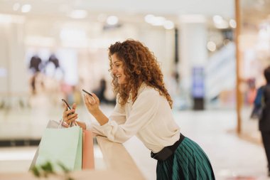 Gülümseyen bir kadının akıllı telefonunu internet üzerinden satış tekliflerini kontrol etmek için kullanması veya alışveriş merkezinde alışveriş yaparken indirim uygulaması kullanması..