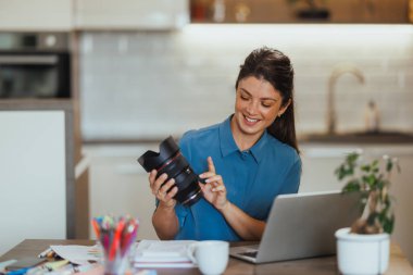 Kadın fotoğraf ürünleri hakkında blog yazıyor ve evde dizüstü bilgisayarında buluşurken kameraya lens gösteriyor..
