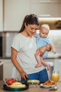 Annem mutfakta sağlıklı yemek yaparken bebeğini kucağında tutarak aynı işi yapıyor..