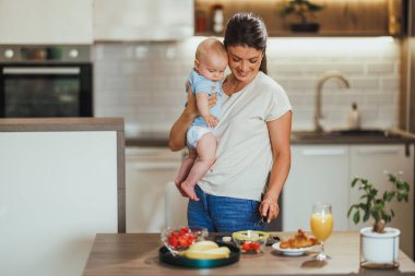 Mutfakta sağlıklı yemek yaparken bebeğini kucağında tutan çok görevli bir anne..