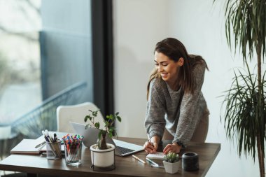 Ev stüdyosunda dizüstü bilgisayarla çalışan yaratıcı genç bir kadın..