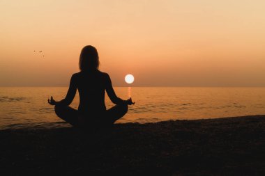 Gün batımında sahilde meditasyon yapan bir kadın silueti..