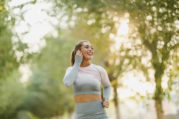 スポーツウェアを着ている幸せな女性は晴れた日に自然の中でジョギングしています ロイヤリティフリーのストック写真