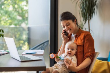 Kadın girişimci, çalışırken ve evde bebeğine bakarken cep telefonuyla iletişim kuruyor..