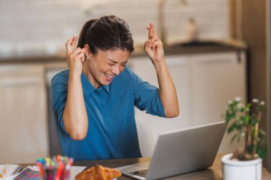 Kadın girişimci, ev ofisinden bilgisayar başında çalışırken gözleri kapalı ve parmakları çapraz olarak beklemektedir..