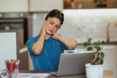 Boyun ağrısı çeken ve evde dizüstü bilgisayar üzerinde çalışırken stres yaşayan serbest çalışan bir kadın..