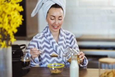 Bornozlu genç bayan kahvaltıya yulaf hazırlıyor..