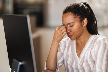 Afrikalı iş kadını baş ağrısı çekiyor ve bilgisayarla uğraşırken endişeli görünüyor.