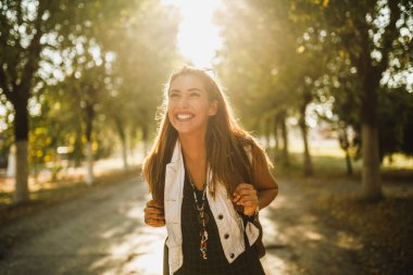 Sırtında sırt çantaları olan genç ve güzel bir kadın güneşli caddede yürüyor ve başka tarafa bakıyor..