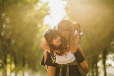 İki güzel neşeli kız arkadaş güneşli caddede yürürken eğleniyor ve sırtımda gezintiye çıkıyorlar..