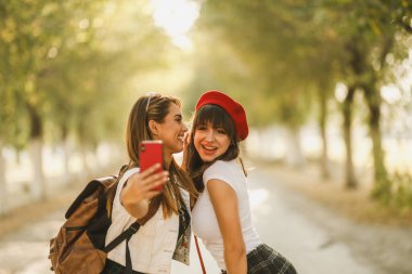 İki güzel kız arkadaş eğleniyor ve güneşli caddede selfie çekiyorlar..