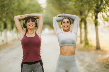 Mutlu iki bayan arkadaş cadde boyunca koşmadan önce esneme egzersizleri yapıyor..