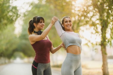 Mutlu iki genç kadın cadde boyunca koştuktan sonra esneme egzersizleri yapıyor..