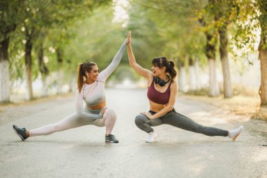 Mutlu iki bayan arkadaş cadde boyunca koştuktan sonra esneme egzersizleri yapıyor..