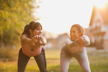 Mutlu iki bayan arkadaş güneşli bir günde doğada esneme egzersizleri yapıyorlar..