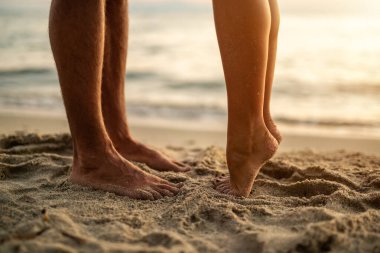 Tanımlanamayan bir çiftin çıplak ayakla kumsalda sarılıp öpüşürken görüntüsü..