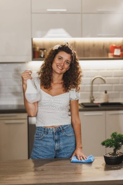 Evde temiz anti bakteriler için elinde bez ve sprey deterjan tutan mutlu bir temizlikçinin portresi. Kameraya bakıyorum..