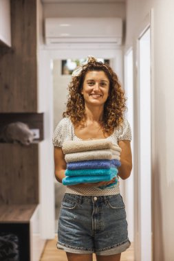 Güzel, gülümseyen bir kadın koridorda duruyor ve evde günlük işlerini yaparken bir yığın havlu tutuyor.. 