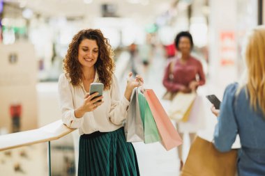 Cep telefonuyla mesajlaşan ve alışveriş merkezindeki alışveriş torbalarını tutarken gülümseyen mutlu bir kadının portresi..
