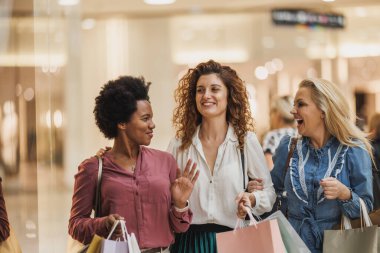 Bir grup neşeli, çok kültürlü kadın canlı bir alışveriş merkezinde perakende terapi ve moda anlayışını kucaklıyor..
