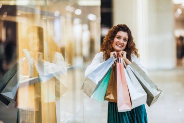 Çanta tutan ve alışveriş merkezinde alışveriş yaparken kameraya bakan çok mutlu bir kadının portresi..