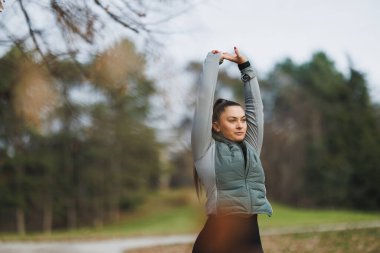 Bir kadın yoga yapıyor ve kollarını doğayla çevrili huzurlu güzel bir parkta açıyor..