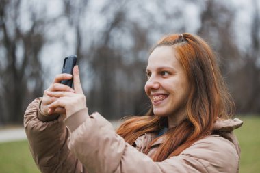Telli bir kadın cep telefonu tutuyor ve fotoğraf çekiyor..