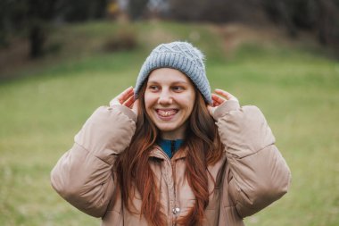 Dişlerinde ortodontik diş teli ve uzun saçlı bir kadın, doğada günün tadını çıkarırken gri bir şapka giyerken yakalandı..