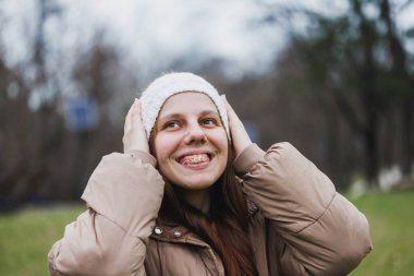 Açık havada duran kahverengi ceketli ve beyaz şapkalı bir kadın..