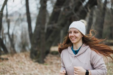 A smiling young woman with orthodontic braces on her teeth in motion, running through a city park in autumn. clipart