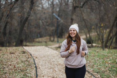 Beyaz bereli bir kadın aktif olarak şehir parkında koşuyor..
