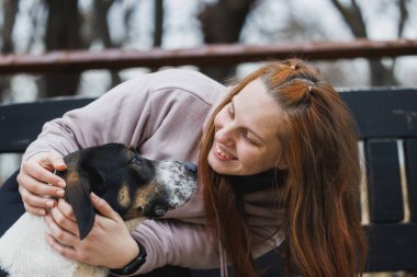 Parktaki bir bankta sakince oturan bir kadın sevgiyle köpeğini kucağına alır..