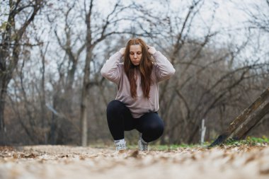 Bir kadın şehir parkındaki eğitimden önce yaprakların üzerine çömeliyor..