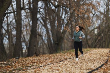 Aktif bir kadın güneşli bir sonbahar gününde yaprak kaplı parkta neşeyle koşar..