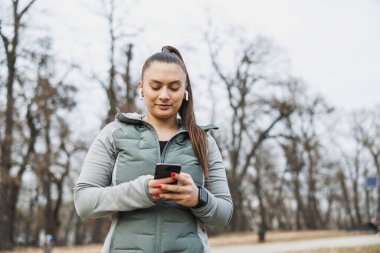 Bir kadın parkta duruyor, kendini cep telefonuna kaptırmış, çevresinden kopuk..