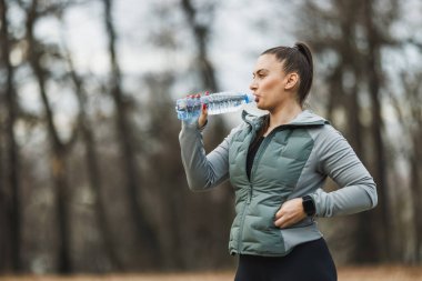 Plastik şişeden su içen genç bir kadın ideal sağlık için susuz kalmamanın önemini vurguluyor..