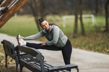 Rahatlatıcı bir açık hava ortamında bacaklarını bir bankta açan odaklanmış genç bir kadın..