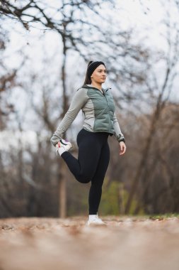 Bir kadın parkta sakin ve odaklanmış bacak esnetme egzersizi yapıyor, esnekliği teşvik ediyor ve gerginliği azaltıyor..