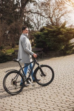 Sıradan bir iş adamı, bisikletiyle tuğla bir yolda yürüyor ve şehir parkında güneşli bir günün tadını çıkarıyor..