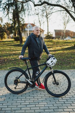 Son sınıftan bir adam bisikletiyle tuğla bir yolda yürüyor ve şehir parkında güneşli bir günün tadını çıkarıyor..