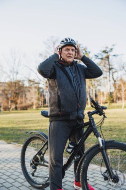 Son sınıf öğrencisi bisikletle parkta duruyor. Bir miğfer tutuyor, güvenli bir yolculuğa çıkmaya hazır ya da yeni bitirmiş..