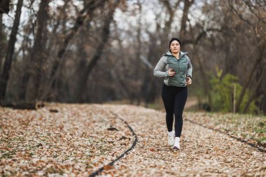 Bir kadın parkta koşuyor, dışarıda spor yapıyor ve spor yapıyor..