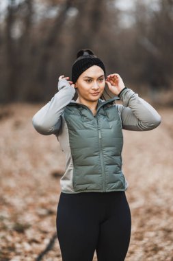 Kendine güvenen genç bir kadın kış sabahı koşusu sırasında saçbandını ayarlamak için kısa bir ara verir..