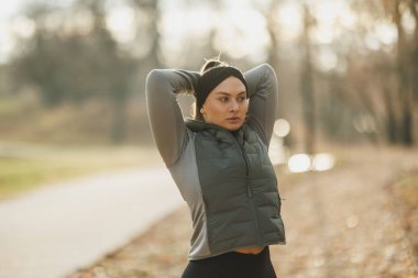 Parkta kollarını uzatan bir kadın, çevresi doğa ile çevrili sağlıklı ve aktif bir yaşam tarzını kucaklıyor..