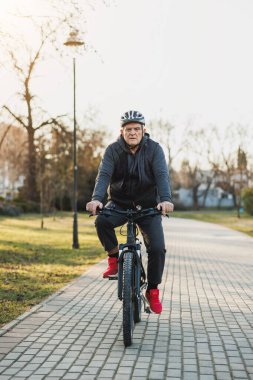 Kask takan son sınıf öğrencisi şehir parkında bisiklet sürüyor..