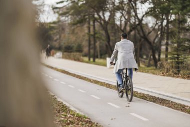 Bir adamın arkadan görünüşü bisiklet yolu boyunca bisiklet sürmekten zevk almaktır, ilerideki yola odaklanmıştır, elleri gidonun üzerindedir..